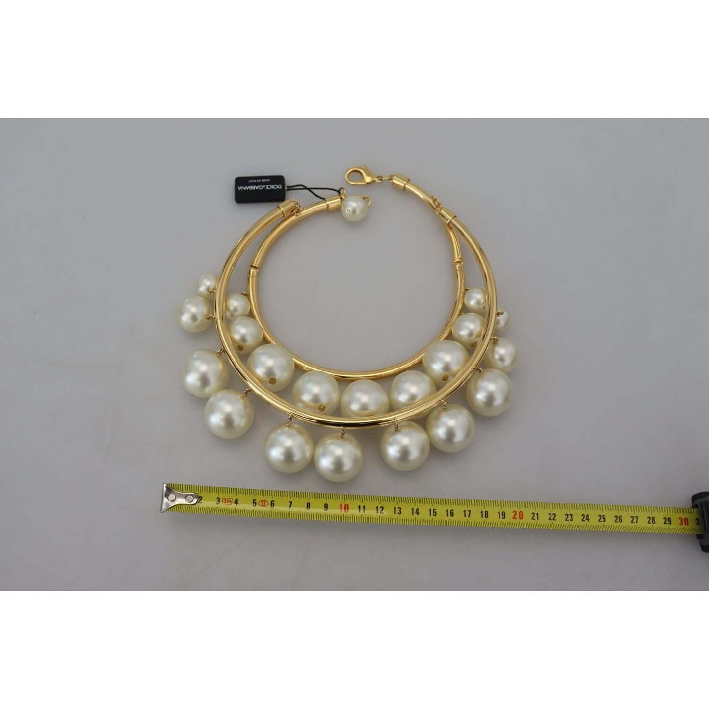 Dolce & Gabbana gold choker with faux pearls and lobster clasp; luxurious accessory on gray background with measuring tape.