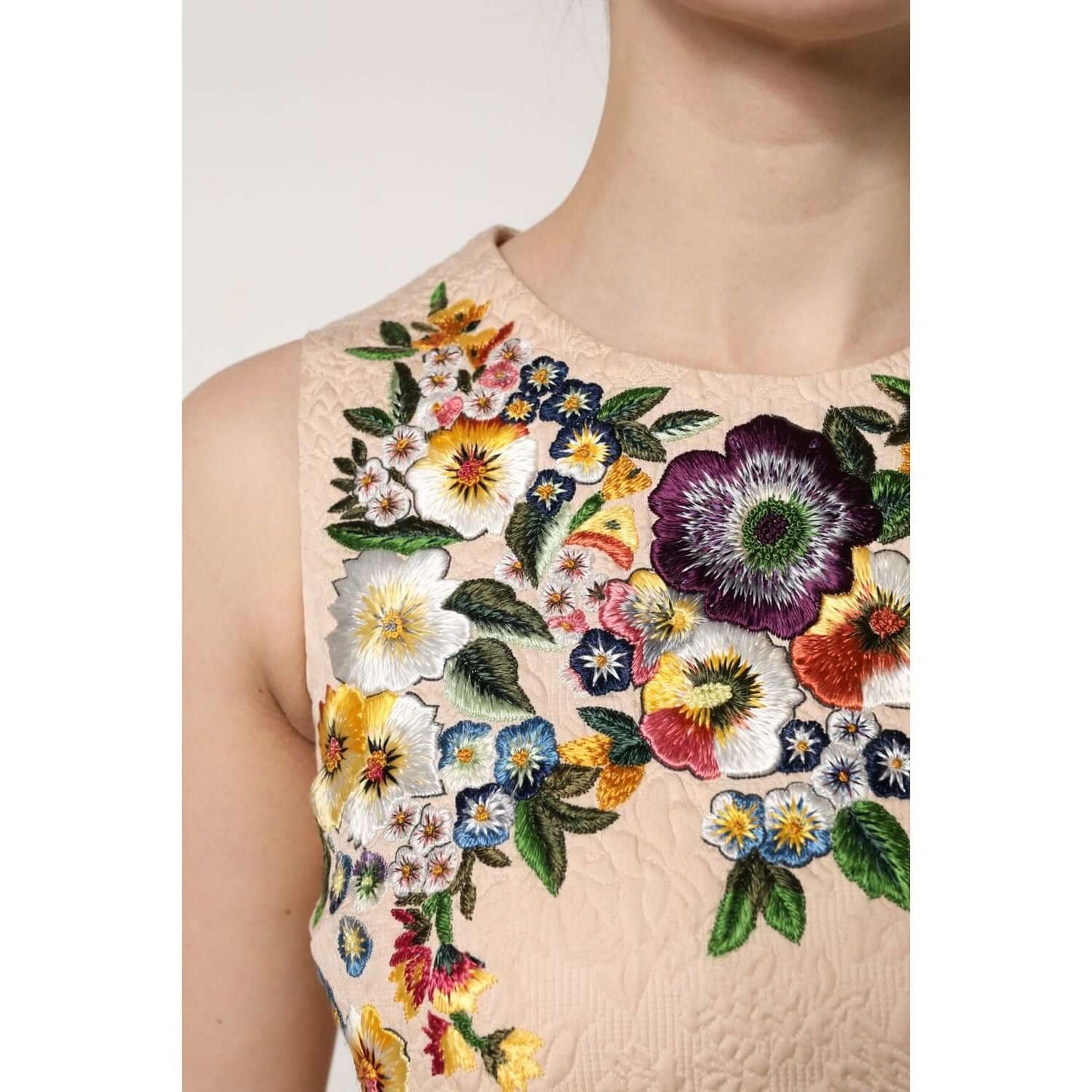 Woman wearing Dolce & Gabbana beige sleeveless top with colorful floral embroidery, showcasing luxury Italian craftsmanship.