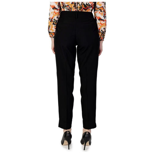 Rear view of women's black cigarette pants made from recycled polyester, part of autumn/winter collection, worn with patterned blouse.
