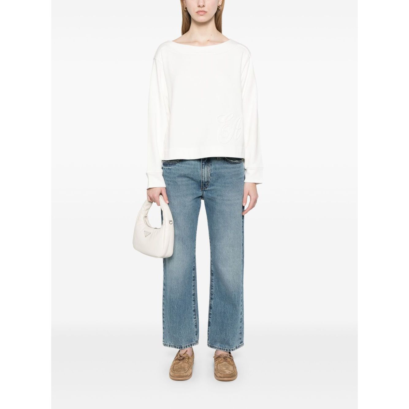 Model wearing Emporio Armani logo embroidered sweatshirt, white crew neck, organic cotton, paired with jeans and holding a small white bag.