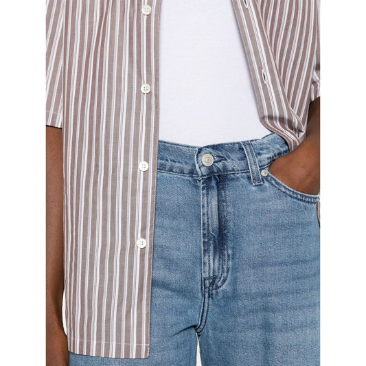Person wearing Seven Jeans Blue, light denim with button fastening and logo patch, paired with striped shirt and white top.