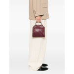 Person holding Stella McCartney Falabella Tiny crossboydy bag in bordeaux red with chain-link handles and logo charm, stylish accessory.